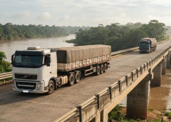 Caminhão de carga atravessa uma ponte rodoviária de concreto sobre um rio cercado pela vegetação amazônica.