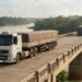 Caminhão de carga atravessa uma ponte rodoviária de concreto sobre um rio cercado pela vegetação amazônica.