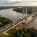 Representação da ponte binacional sobre o Rio Mamoré, com estrutura estaiada, caminhões e acessos rodoviários entre Brasil e Bolívia.
