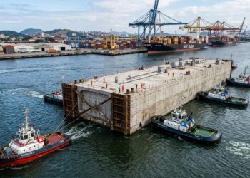 Módulo de concreto do túnel é rebocado flutuando pelo canal de Santos.