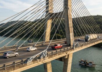 Detalhe do trecho estaiado de uma ponte, com cabos de aço diagonais conectando o tabuleiro a uma torre de concreto sobre a baía.