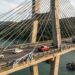 Detalhe do trecho estaiado de uma ponte, com cabos de aço diagonais conectando o tabuleiro a uma torre de concreto sobre a baía.