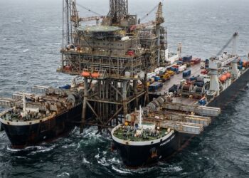 Navio Pioneering Spirit posicionado ao redor da estrutura superior de uma plataforma petrolífera em alto-mar.