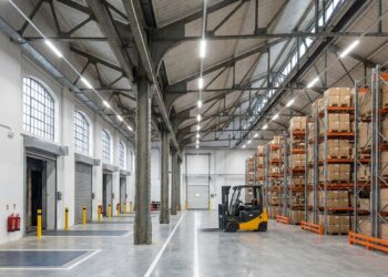 Interior de antiga fábrica adaptada para armazenagem com estantes para paletes, empilhadeira e corredores logísticos.