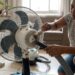 Mulher limpa com pincel as entradas de ar da carcaça do motor de um ventilador desligado.