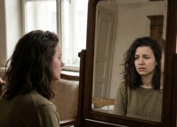 Mulher observando o próprio reflexo no espelho, em uma cena que representa a relação entre autoimagem e percepção pessoal.