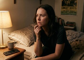 Mulher sentada na cama à noite, refletindo sobre uma conversa que teve durante o dia.