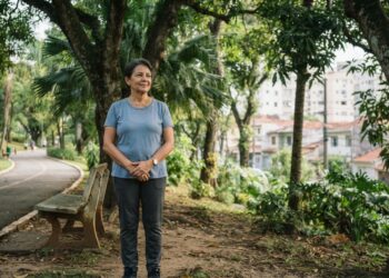 Mulher de 60 anos faz uma pausa durante a caminhada e observa as árvores em um parque urbano brasileiro.