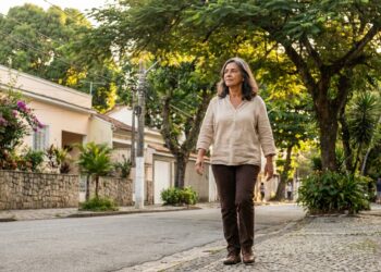 Mulher brasileira madura caminha sozinha por uma rua tranquila e arborizada, aproveitando um momento de liberdade e reflexão.