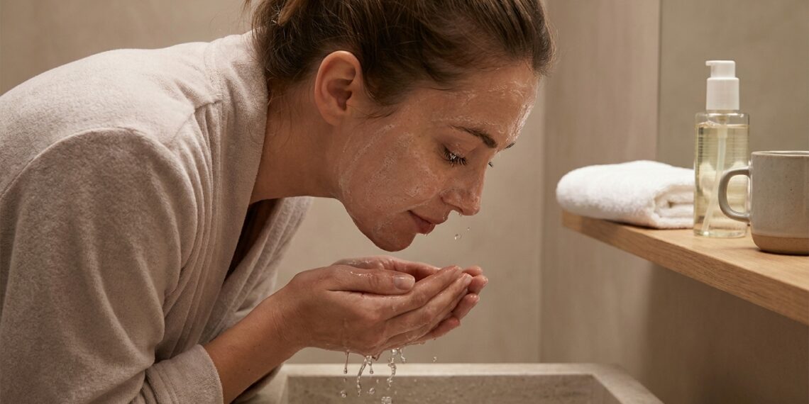 Mulher lavando o rosto antes de dormir para remover maquiagem, protetor solar e resíduos acumulados durante o dia.