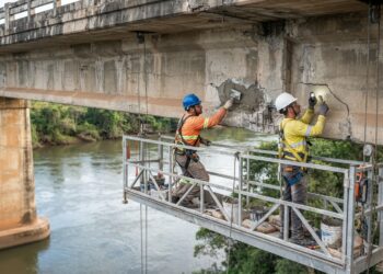 Técnicos realizam reparos localizados em uma viga de concreto sob uma ponte rodoviária sobre o Rio Doce.