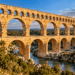 Aqueduto romano Pont du Gard, na França, com seus arcos monumentais de pedra atravessando um vale sobre um rio.
